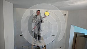 Dirty plasterer man polish ceiling with sanding grinder machine