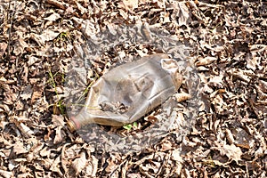 A dirty plastic and glass bottle left in the autumn forest.