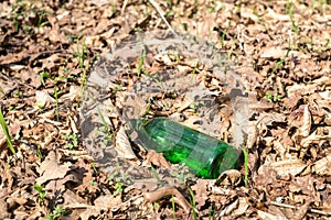 A dirty plastic and glass bottle left in the autumn forest.