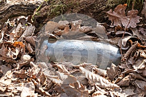 A dirty plastic and glass bottle left in the autumn forest.