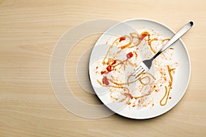 Dirty plate with food leftovers and fork on wooden background. Space for text