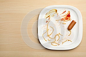 Dirty plate with food leftovers and sausage on wooden background. Space for text