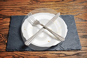 Dirty plate with knife and fork crossed on the dark board on the wooden background