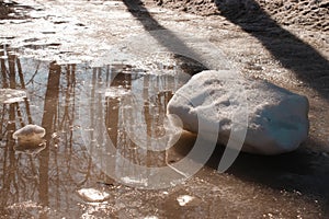 A dirty puddle of a melted snow. A big chunk of white snow is on the right and a smaller piece on the left. A dark picture with