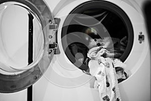 Dirty pyjamas with grey heart print hangs from open door of washing machine