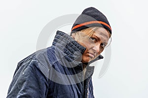 Dirty, sad homeless woman 30-40 years old, against a gray sky