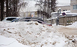 Dirty snowdrift by the road against the backdrop of a city street with cars.