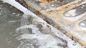 Dirty soapy water drains the kitchen sink. Sewage flows into the sewer through a steel grate