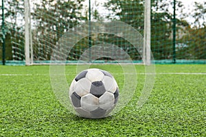 Dirty soccer ball on green football field against net