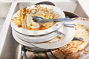 Dirty stack of unwashed oily dishes plates in wash basin photo