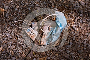 A dirty surgical mask lies on a dirt road and pollutes the environment