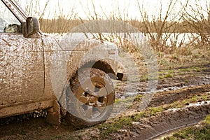 Dirty SUV is driving off-road with puddles and dirt close-up.