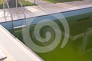 Dirty Swimming Pool with Green Water. A close-up view of a neglected swimming pool with murky green water, reflecting its photo