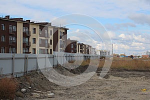 A dirty wasteland behind a fence near high-rise buildings in a ghetto on the outskirts of the city depressive