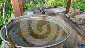 Dirty water from the well. Ecology of the planet. Woman drops chain with bucket into rustic well to draw water.