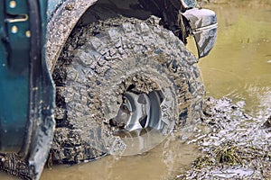 The dirty wheel of a 4x4 off-road car is half drowned in a puddle