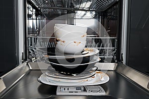 Dirty white and black plates, standing in front of an open dishwasher