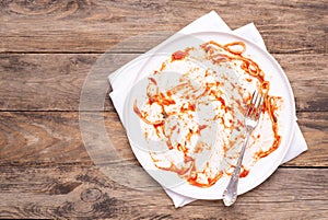 Dirty white plate with leftovers on wooden table, top view