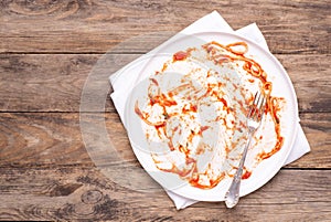 Dirty white plate with leftovers on wooden table, top view photo