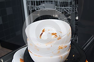 Dirty white plates, standing in front of an open dishwasher