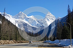 Dirty white SUV drives along a scenic highway running under the snowy mountains