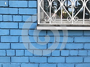dirty white window with a grille against the background of a blue brick wall.