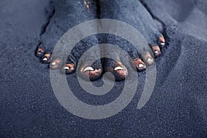 Dirty woman bare feet in black sand