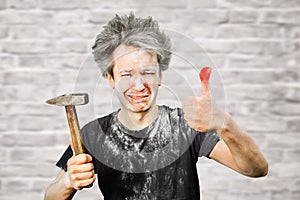 Dirty young builder guy fail is hold a hammer, hit the finger on brick wall background at home during repairs photo