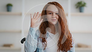 Disability and positive. Cute little disabled redhead girl in wheelchair and waving hand to camera, saying hello to