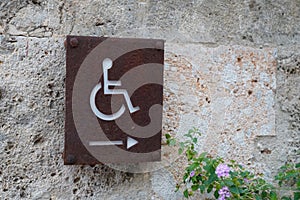 Disabled accessible arrow entry sign post with wheelchair handicap logo pointing side on wall entrance store access pictogram on