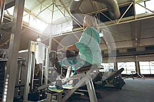 Disabled active senior woman exercising with leg curl machine in fitness studio