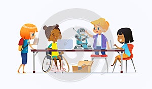 Disabled African American girl in wheelchair and other children standing around desk with laptops and robot and working