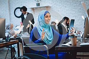 Disabled arab woman in wheelchair working in office. Woman is talking on tablet.