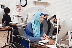 Disabled arab woman in wheelchair working in office. Woman is working on desktop computer.