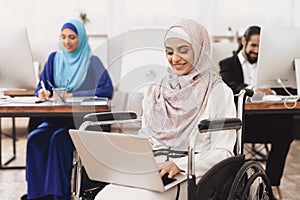 Disabled arab woman in wheelchair working in office. Woman is working on laptop.
