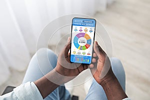 Disabled black man using smartphone, counting spendings, top view