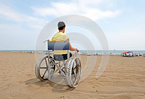 Disabled boy sitting on a wheelchair  facing the sea
