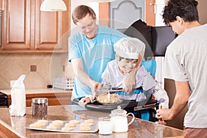 Disabled boy in stander baking cookies with father and brother