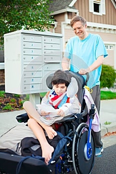 Disabled boy in wheelchair getting mail from mailbox with father