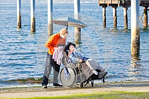 Disabled boy in wheelchair with his caregiver on beach