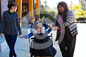 Disabled boy in wheelchair holding hands with caregivers on walk