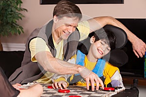 Disabled boy in wheelchair playing checkers with father at home