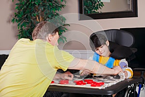 Disabled boy in wheelchair playing checkers with father at home