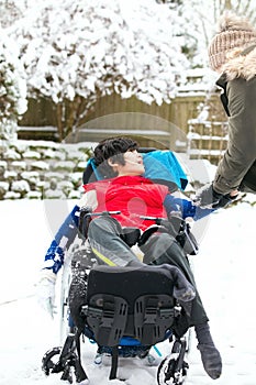 Disabled boy in wheelchair playing with snow in winter