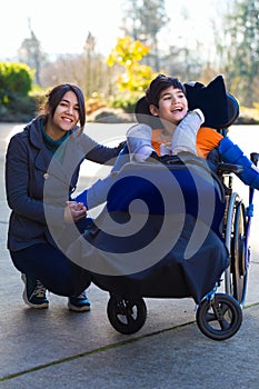 Disabled boy in wheelchair sitting with his caregiver outdoors