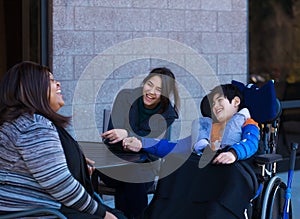 Disabled boy in wheelchair at table outdoors talking with caregivers