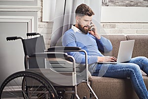 Disabled businessman sitting on a couch, working on a laptop, talking on a phone