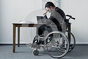 Disabled businessman sitting in wheelchair at workplace with bowed head
