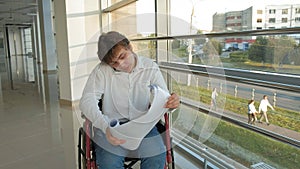 A disabled businessman on a wheelchair in a window with a drawing on a large sheet of paper, discusses work by phone