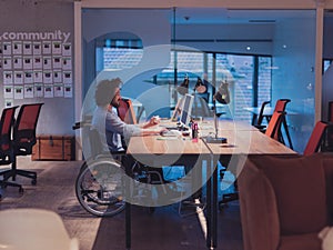 Disabled businessman in wheelchair working overtime alone at his desk in an office late at night